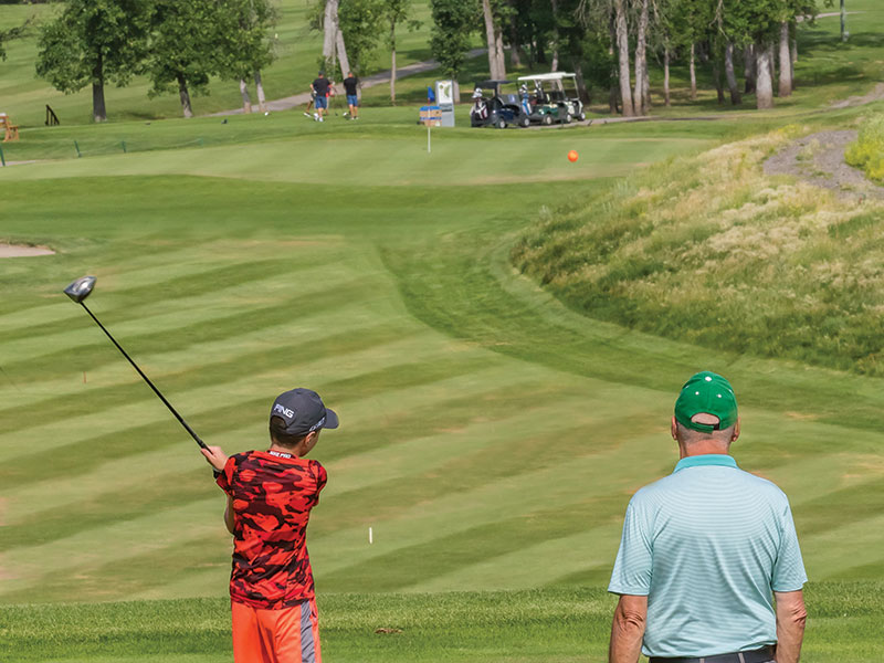 A junior player swings at the ball while another golfer looks on at Wheat City Golf Course, Brandon, Manitoba